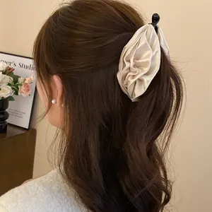 Elegante fermaglio per capelli con fiore in tessuto beige plissettato visto in dettaglio.