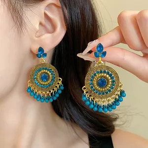 Detail view of ethnic gold dangle earrings with blue rhinestones and turquoise bead tassels