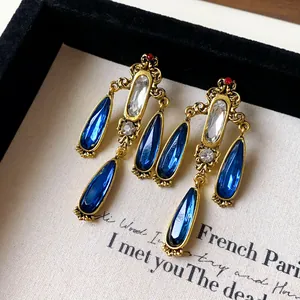 Close-up of vintage gold-tone earrings with blue water-drop tassels and clear gems.