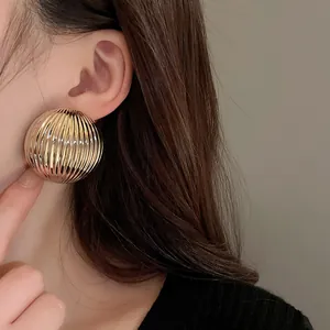 Macro view of minimalist golden metallic striped semi-round earrings on a model's ear