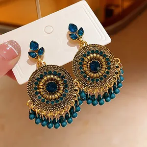 Detail view of ethnic style gold earrings with blue rhinestones and bead tassels