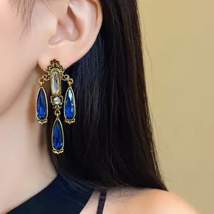 Close-up of vintage gold earrings with sparkling blue teardrop crystals and royal style