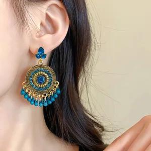 Detail showing ethnic gold earrings with blue rhinestones and bead tassels on ear