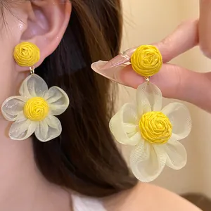Vista detallada de pendientes de flor de rafia amarilla y gasa usados por una modelo