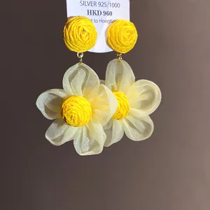 Primer plano de pendientes de flores de rafia amarilla y gasa con agujas de plata