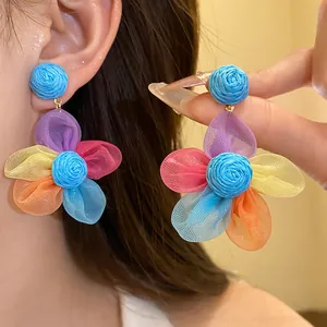 Primer plano de pendientes colgantes de flores de gasa con centro de rafia azul tejido