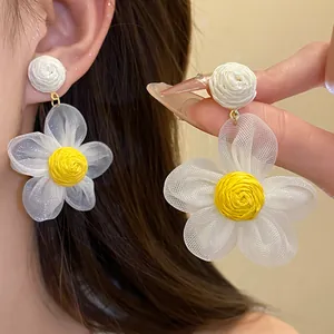 Detalle de pendientes de flores de gasa blanca con centro de rafia amarilla tejida.