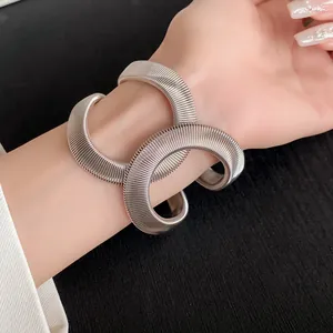 Primer plano de un brazalete elástico cruzado en espiral plateado puesto en la muñeca
