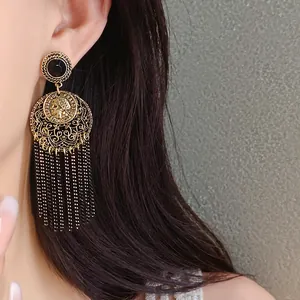 Close-up of a vintage-style gold tassel earring with a French coin motif on a model.