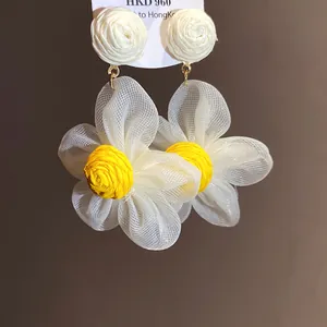 Primer plano de pendientes de flor de gasa blanca con centro de rafia amarilla texturizada