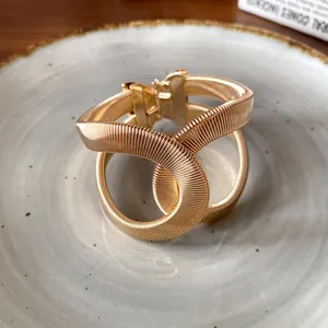 Primer plano de un brazalete de serpiente cruzado dorado con textura elástica.