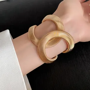 Primer plano de un brazalete elástico cruzado de estilo serpiente dorado en la muñeca