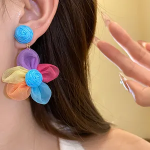 Vista detallada de pendientes de flores de rafia y gasa de colores en la oreja de modelo