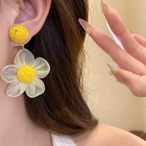 Vista macro detallada de pendientes flor de rafia amarilla con pétalos de gasa blancos