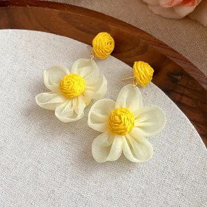 Primer plano de los pendientes de flores de rafia amarilla y gasa blanca sobre tela