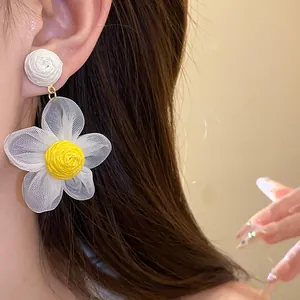 Primer plano de pendientes florales de rafia y gasa con pétalos de malla blanca y núcleo amarillo