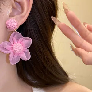 Detalle de un pendiente de flor de rafia y gasa rosa hecho a mano en la oreja