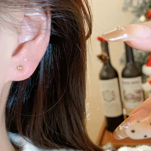 Detailed macro view showing a minimalist round gold ball stud earring worn on an ear