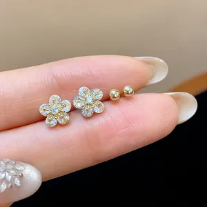 Macro view of zircon flower earrings and gold ball studs held between fingers.