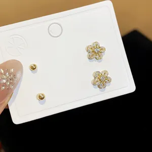 Detail view of sparkling zirconia flower stud earrings and minimalist gold ball studs
