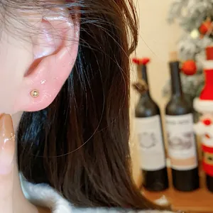 Detailed macro view of a minimalist gold ball stud earring worn on an ear with festive background