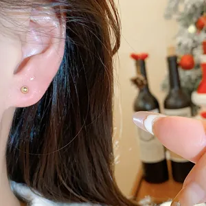 Close-up shot of a minimalist tiny gold ball stud earring worn on the earlobe with cozy background