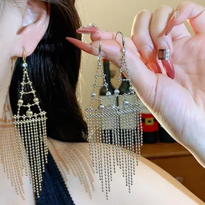 Detalle de elegantes pendientes largos de borla geométrica con circonitas en la oreja.