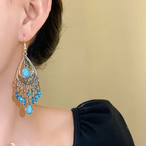 Dettaglio di orecchini etnici bohémien con strass blu e nappine in argento lucido.