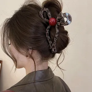 Close-up of vintage leopard print bow hair claw clip with red bead decoration on bun.