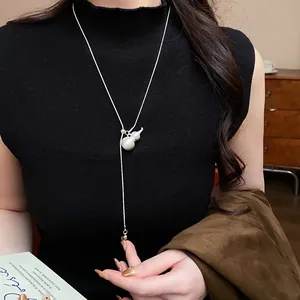 Detailed view of a brushed silver calabash pendant necklace worn on a black turtleneck.