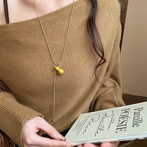 Detail view of a brushed gold gourd pendant necklace worn on a brown knit sweater