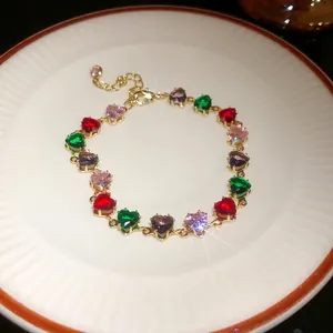 Détail macro d'un bracelet en or orné de zircons multicolores en forme de cœur.
