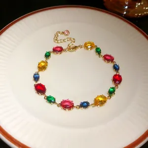 Gros plan d'un bracelet en pierres précieuses colorées sur une assiette blanche, détails dorés.