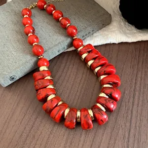 Collar llamativo de acrílico rojo con detalles dorados sobre fondo de madera