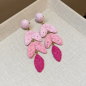 Detailed macro view of pink woven raffia drop earrings with gold-plated connectors