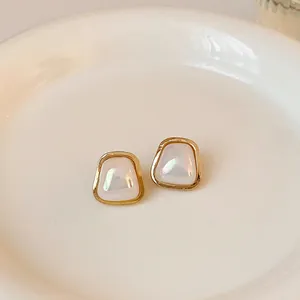 Close-up of geometric trapezoid stud earrings with iridescent pearl-like inlay in gold