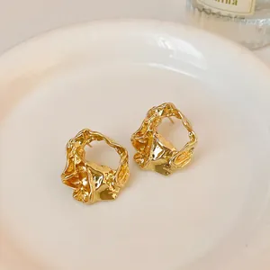 Detailed close-up view of elegant gold-plated crumpled metal stud earrings on a white saucer