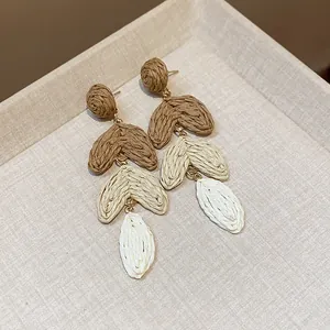 Detailed view of handmade raffia tiered heart leaf earrings in natural brown and beige
