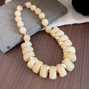 Primer plano detallado de collar de acrílico jaspeado crema con anillos dorados sobre un libro
