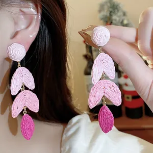 Close-up view of vibrant pink raffia woven drop earrings with silver needle posts