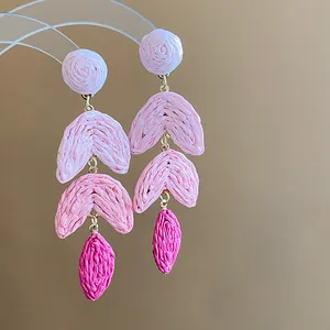 Detail shot of pink gradient raffia woven drop earrings on a clear stand