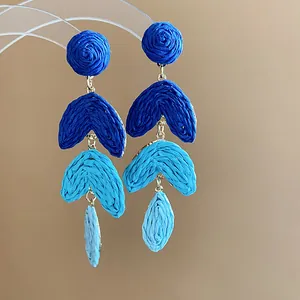 Close-up of handmade raffia woven dangling earrings in a gradient blue palette