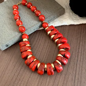 Primer plano de un collar de cuentas de acrílico rojo con detalles dorados sobre un libro.