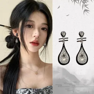 Détail de boucles d'oreilles goutte d'eau avec émail noir et cristaux de style chinois.