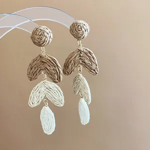 Close-up macro view of bohemian tiered raffia woven leaf earrings in earth tones.