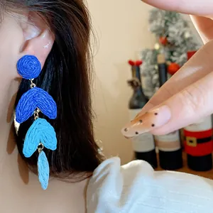 Detailed view of blue gradient raffia drop earrings on model ear, bohemian style
