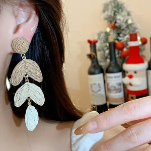 Close-up of three-tiered raffia woven drop earrings worn by a model for Christmas styling.