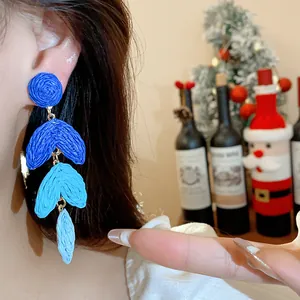 Close-up of blue gradient raffia drop earrings worn on ear with festive background