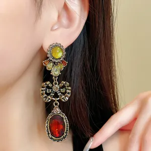 Detailed macro view of vintage bow drop earrings with red and green stones on a model ear
