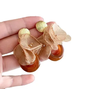 Elegant fabric flower earrings with amber resin ring and gold textured stud on hand